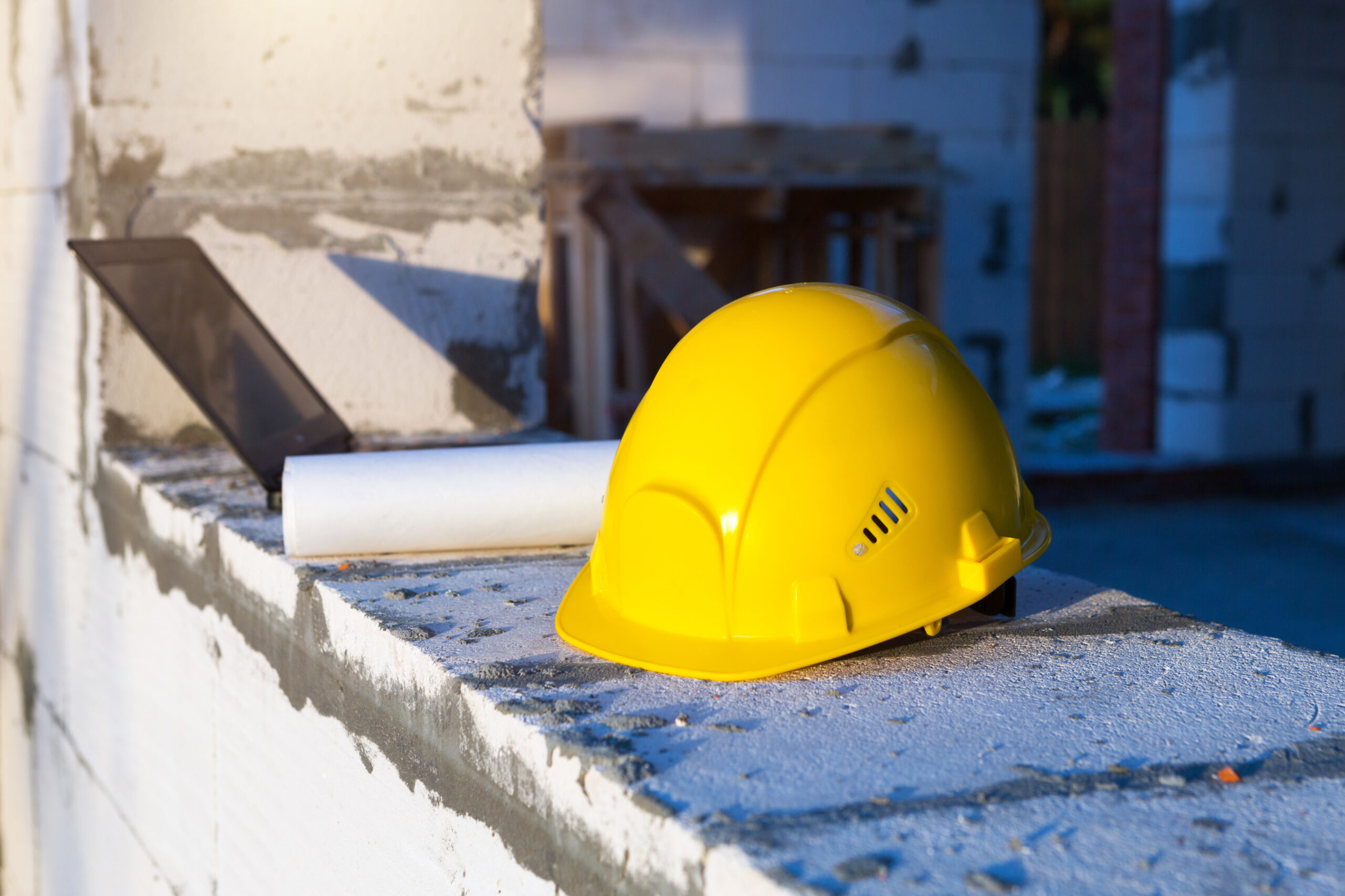Construction hardhat, drawing and laptop on the window of a house under construction. Workflow, architecture and engineering.